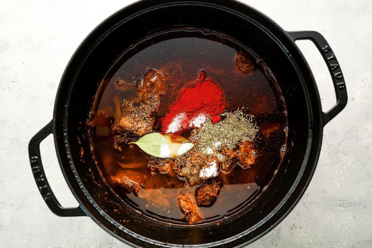 Dutch oven with broth, water, caraway seeds, paprika, thyme, bay leaf, and sugar added to onion and beef mixture