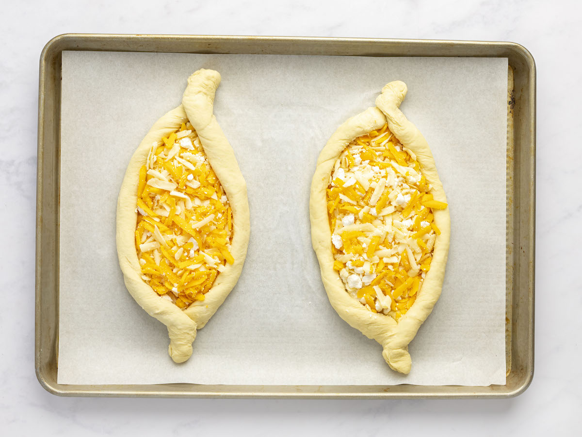 two cheese-filled khachpuri on parchment-lined baking sheet