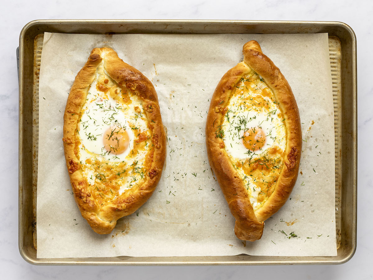 fully baked khachpuri sprinkled with fresh dill on parchment-lined baking sheet