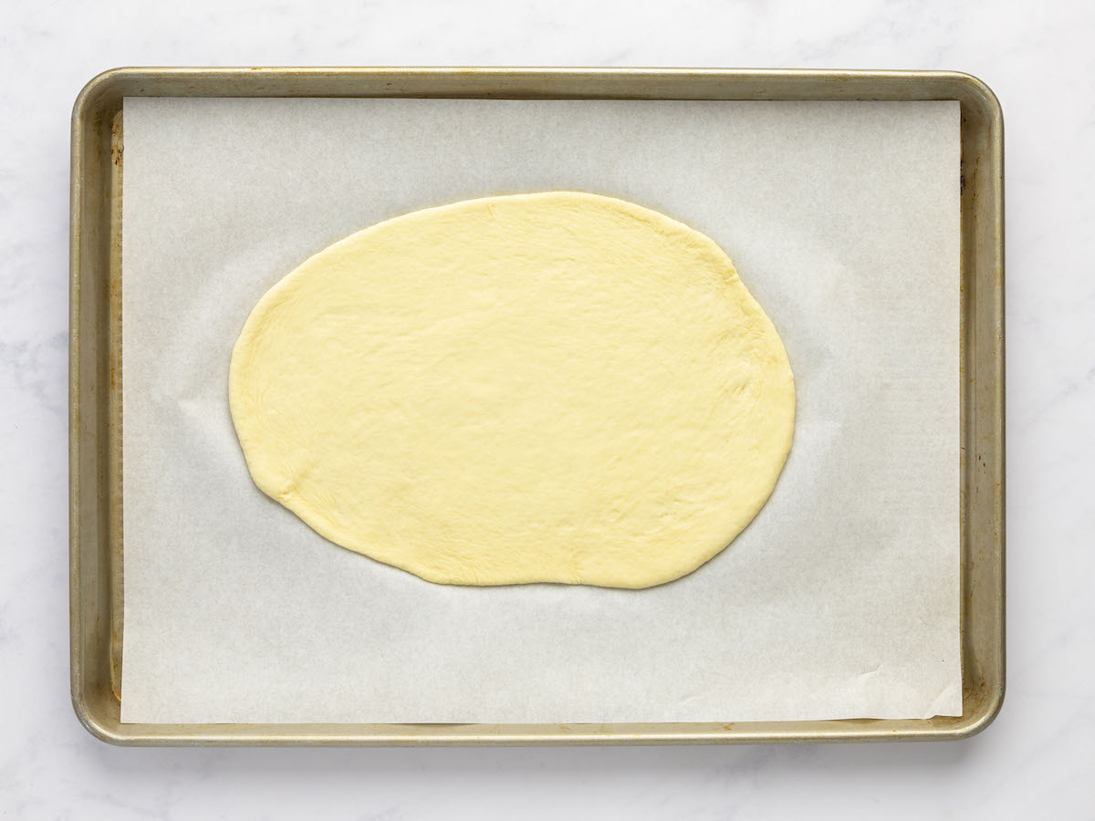 parchment-lined baking sheet with dough ball rolled into oval 