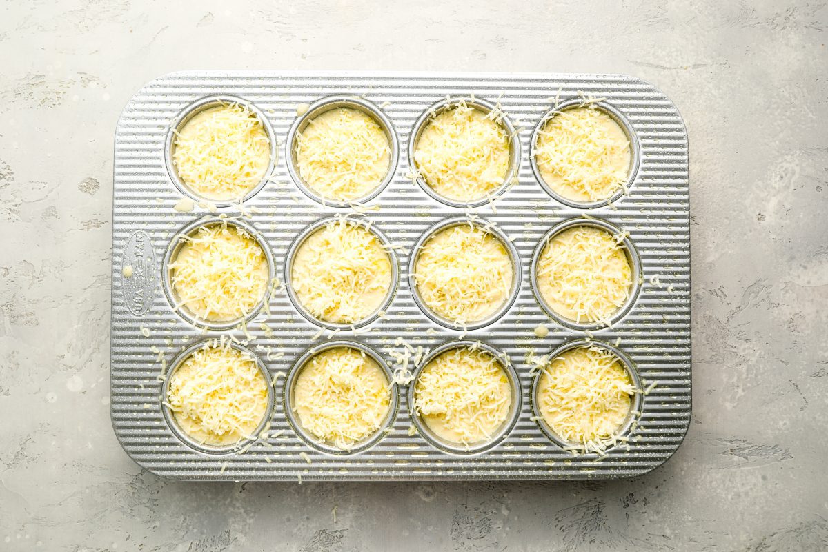 popover batter with cheese sprinkled on top in muffin tin