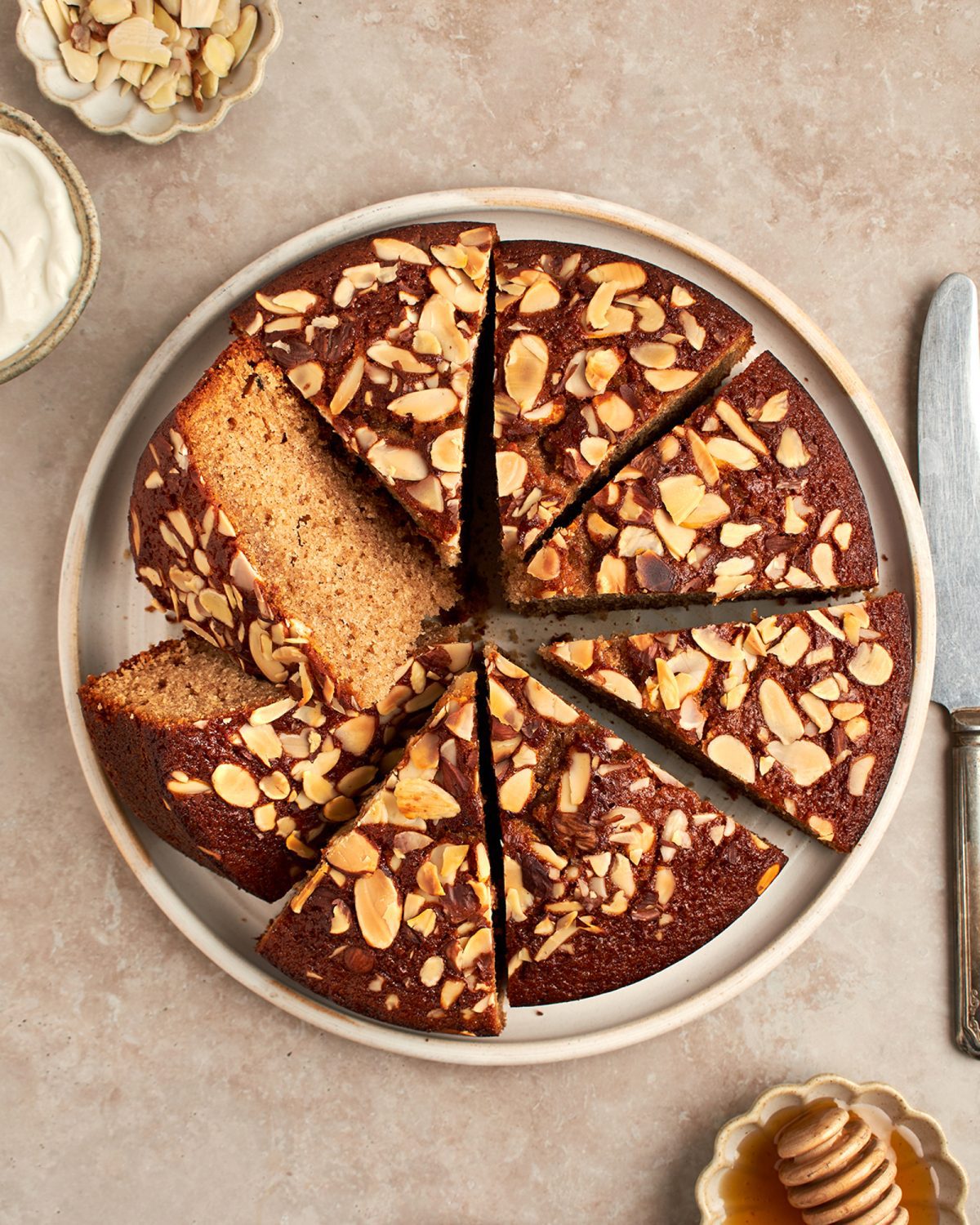 honey cake on platter with bowls of whipped cream, honey and almonds