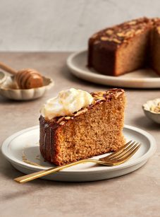 honey cake on platter with bowls of whipped cream, honey and almonds