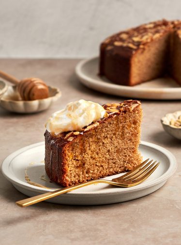 honey cake on platter with bowls of whipped cream, honey and almonds