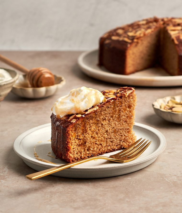 honey cake on platter with bowls of whipped cream, honey and almonds