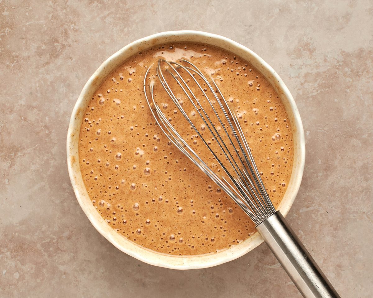 whisked honey cake batter in bowl with whisk