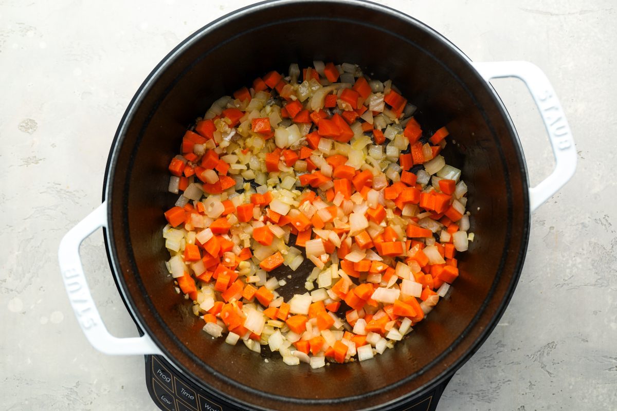 dutch oven with minced garlic, chopped onions, and chopped carrots