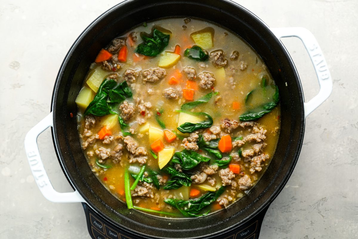 spinach and sausage added to soup in dutch oven