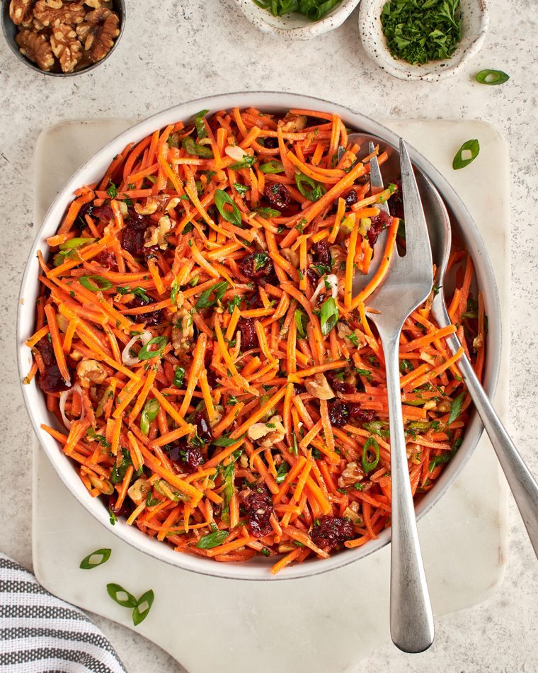 carrot slaw with cranberries, walnuts, and citrus vinaigrette in serving bowl.