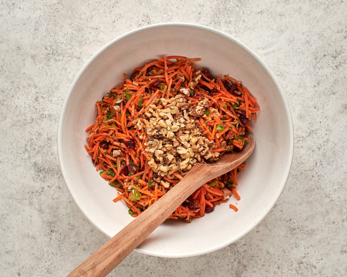 walnuts tossed into  slaw in bowl with wooden spoon