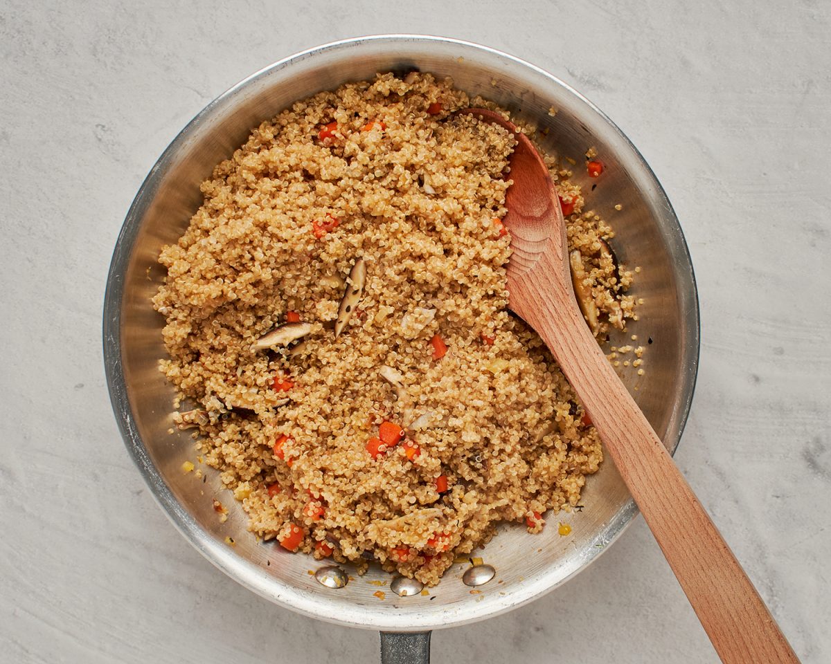 mixing cooked quinoa with vegetables in skillet