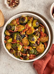 roasted Brussels sprouts with bacon in bowl with serving spoon and linen napkin