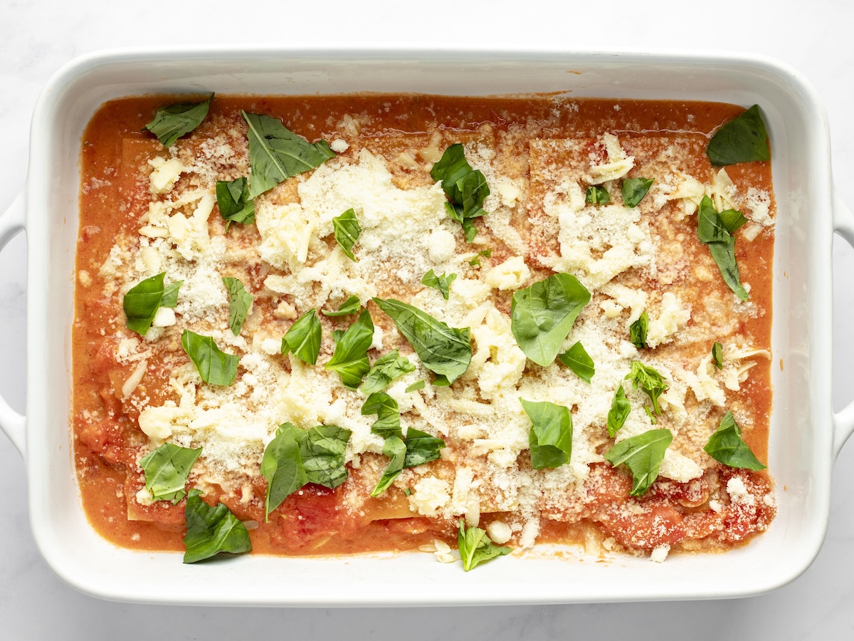 layering cheese lasagna with sauce, noodles, cheese and basil.