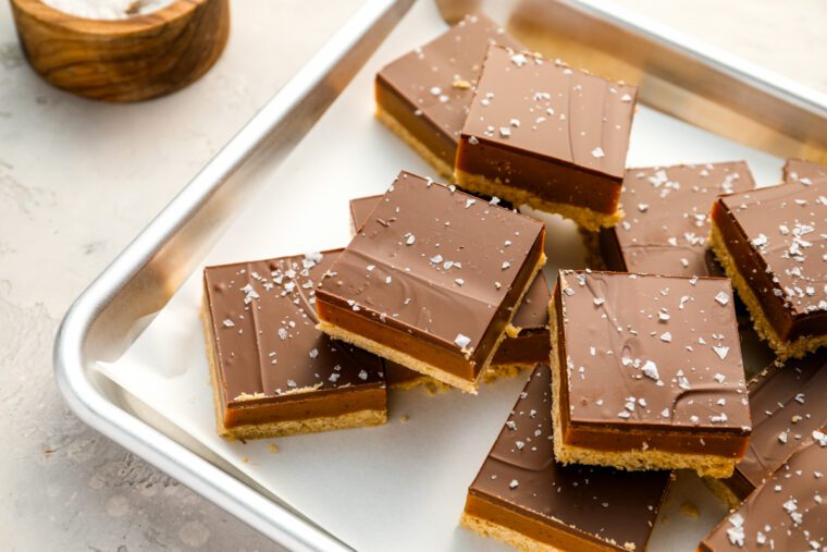 millionaire's shortbread bars on baking sheet with bowl of flaky sea salt.