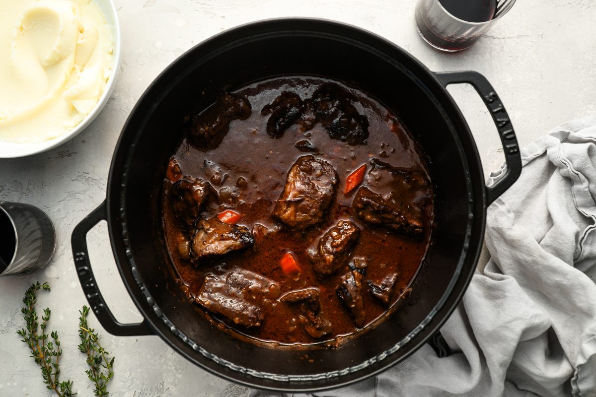 Braised short ribs in Dutch oven with mashed potatoes on the side and glasses of wine.