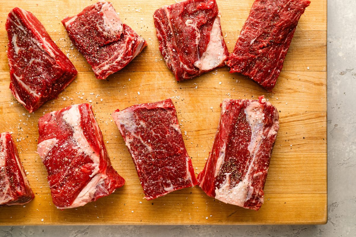 Short ribs seasoned with salt and pepper on cutting board.